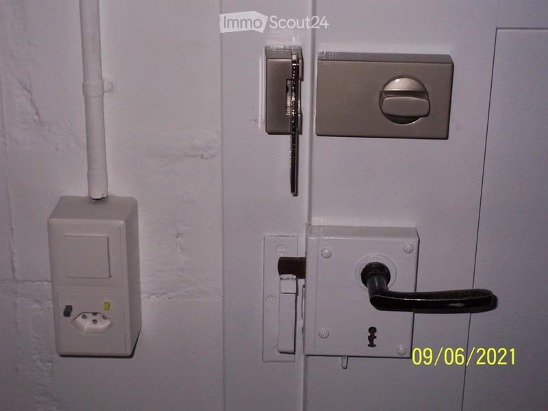 Close-up view of a door with a lock, handle, and electrical outlet on the wall.
