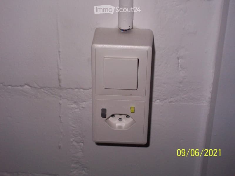 Empty room with a light switch and electrical outlet mounted on a plain wall.