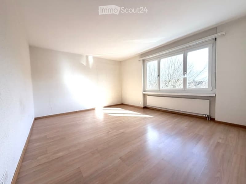Empty room with wooden flooring, white walls, and large windows allowing natural light to enter. No furniture or equipment is present.