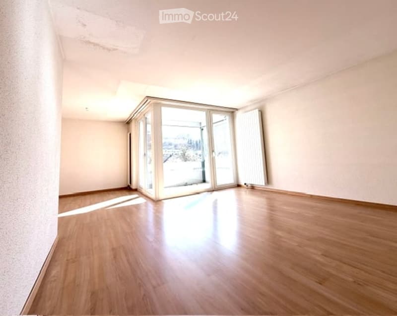 Empty room with wooden flooring, large sliding glass doors leading to a balcony with a scenic view.