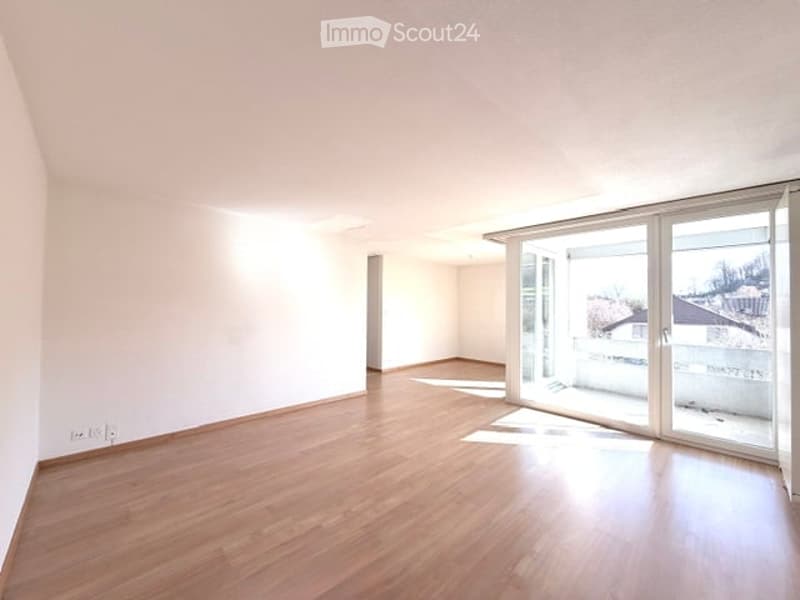 Empty room with wooden flooring, white walls, and large sliding glass doors leading to a balcony.
