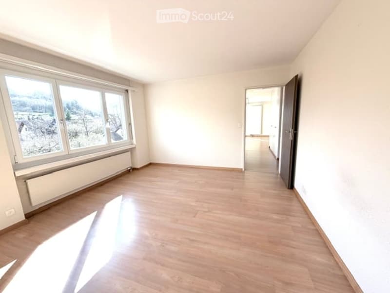 Empty room with wooden flooring, large windows, and a radiator. No furniture or equipment present.