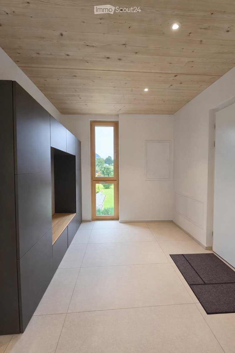 Modern hallway with light wooden ceiling, white walls, tiled floor, and a wooden door leading outside.
