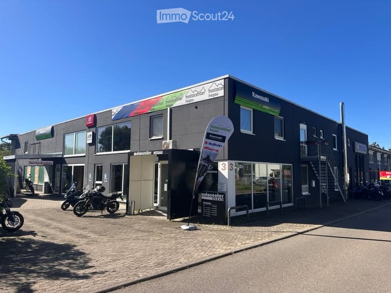 Modern two-story building with large windows and signage for "motocenter hegau" and "Kawasaki". Several motorcycles are parked in front.
