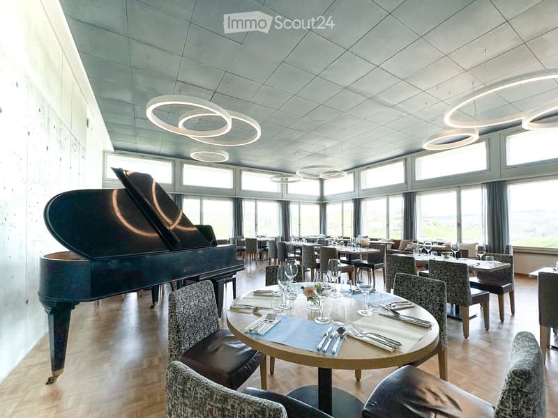 restaurant room with piano, round tables, chairs, wooden floors, ceiling lights, large windows