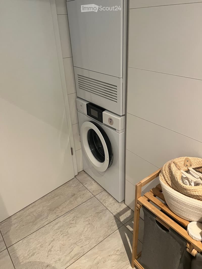 A modern bathroom with a white washing machine, a drying rack, and a wicker basket on a wooden shelf.