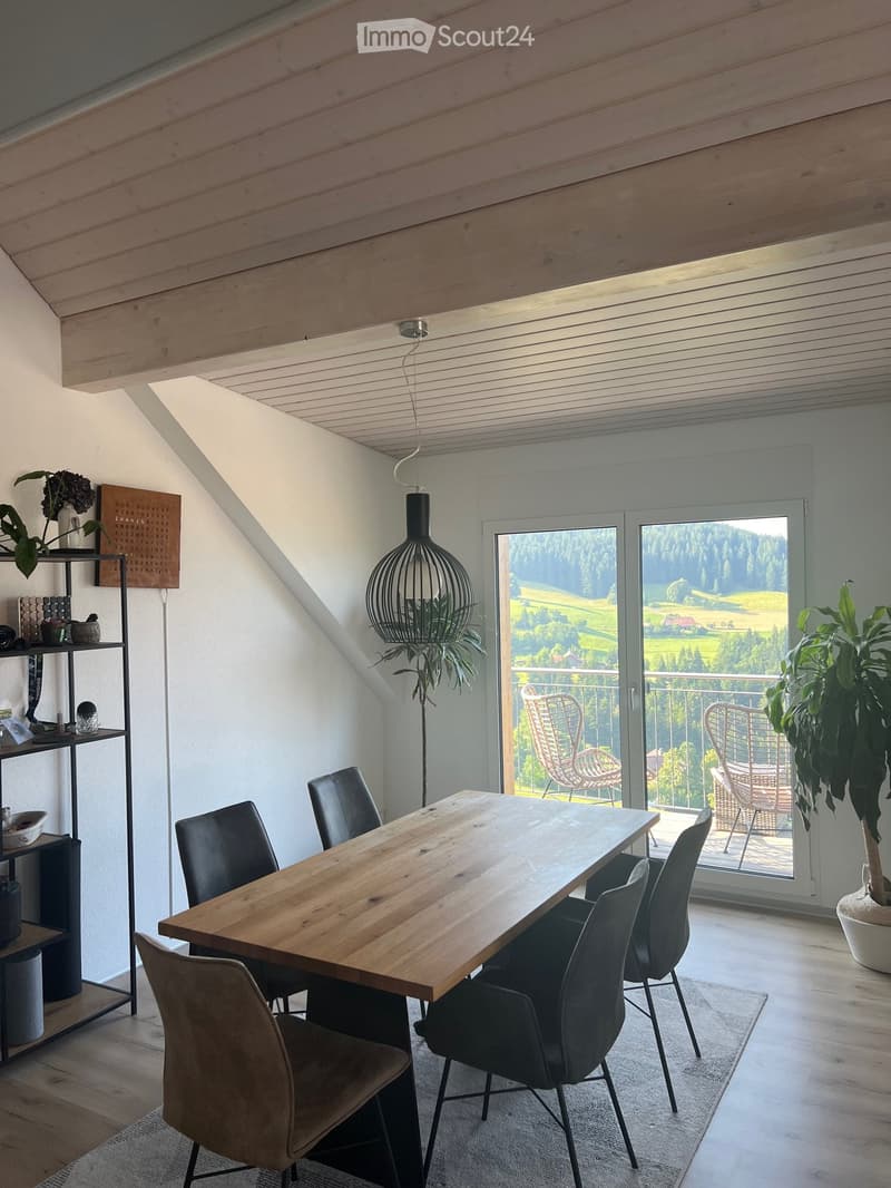 Bright dining area with wooden table, black chairs, modern pendant light, and large window offering scenic view.
