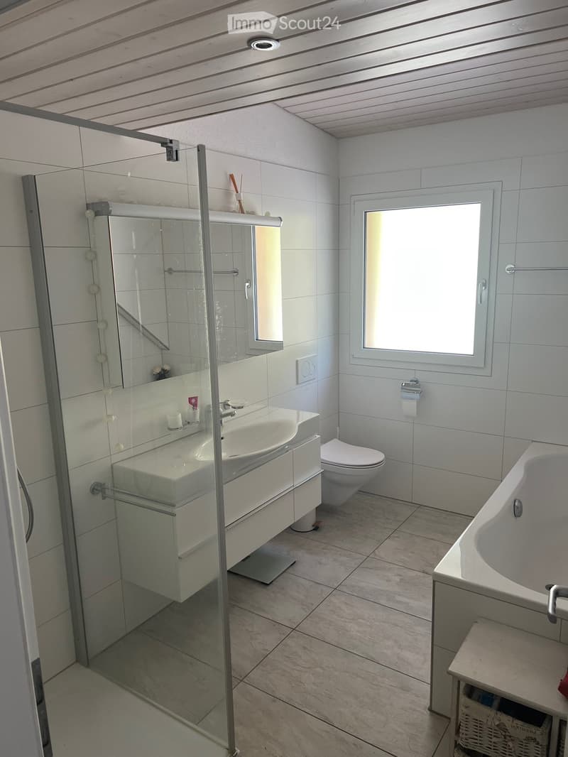 Modern bathroom with white tiles, a large window, a glass-enclosed shower, a sink with a mirror, a toilet, and a bathtub.
