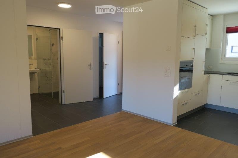 Empty room with wooden flooring, white walls, and a glass shower enclosure visible in the background. No furniture or equipment present.
