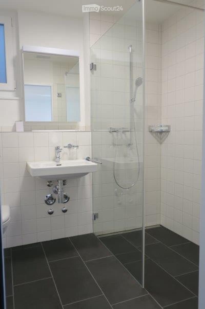 Modern bathroom with white tiles, black floor, white sink, mirror, and glass-enclosed shower.