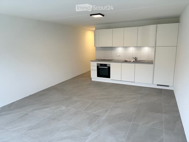 Empty kitchen with white cabinets, stainless steel sink, and built-in oven. Grey tiled floor and white walls.