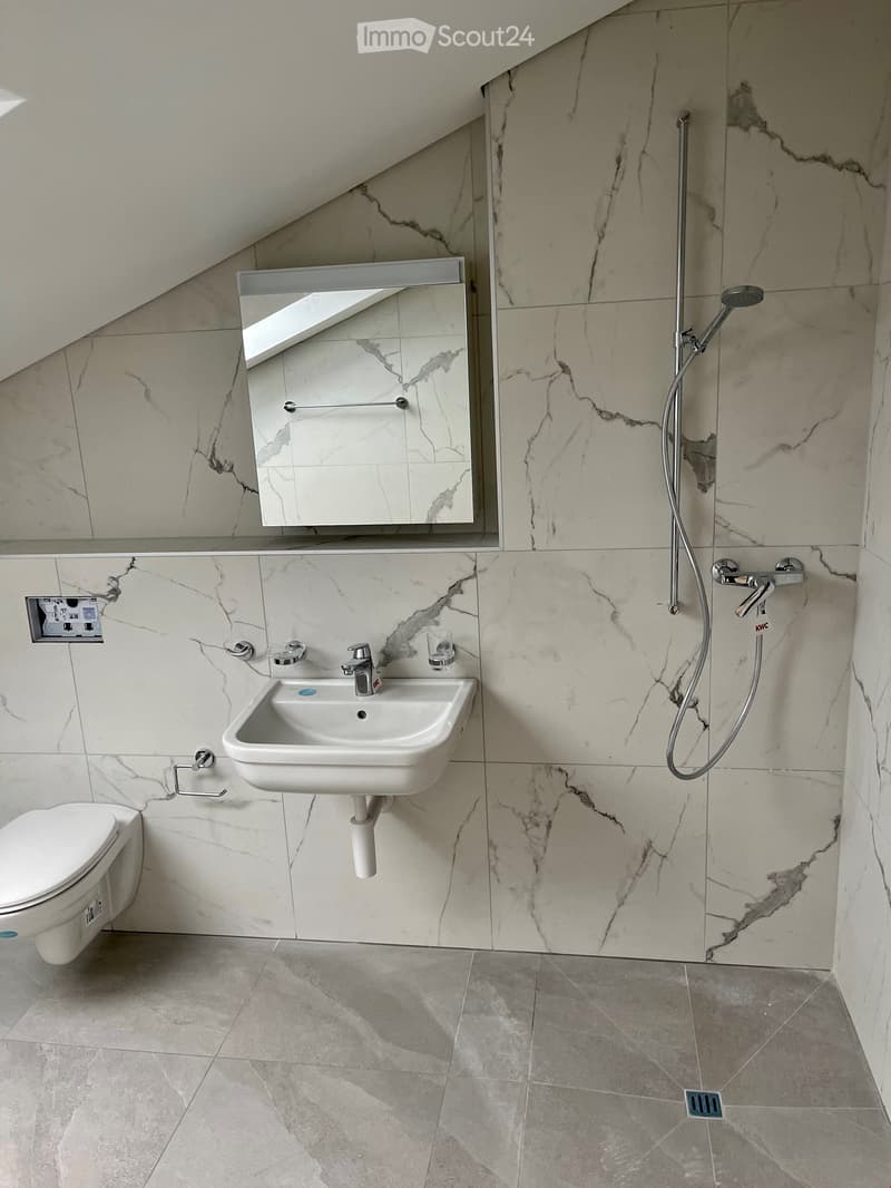 Modern bathroom with marble tiles, a toilet, a sink with a faucet, a mirror, and a shower head.
