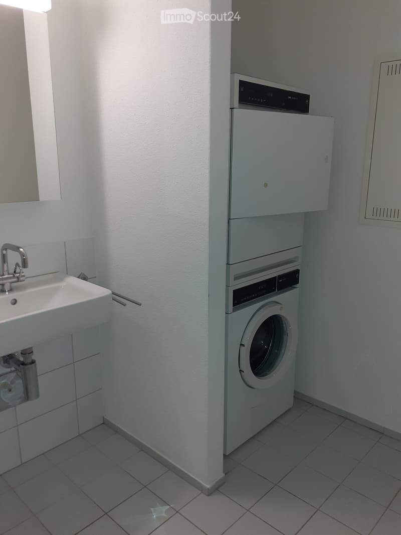 A small bathroom with a white sink, chrome faucet, and a stacked washing machine and dryer unit.