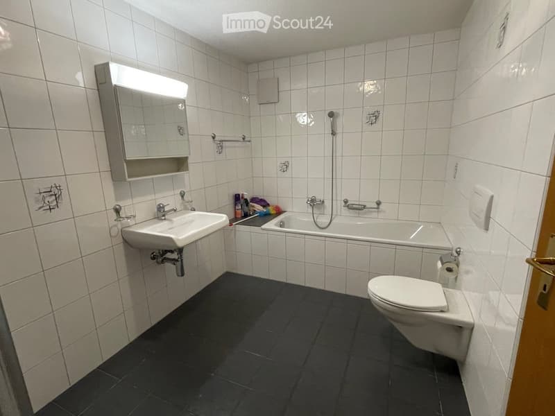 white tiled walls, white sink, white bathtub, white toilet, white mirror, black floor