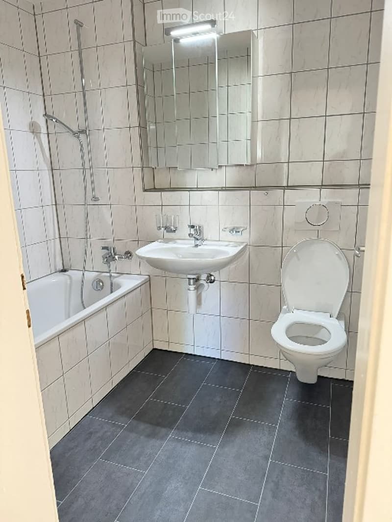 A bathroom with white tiles, bathtub, sink, mirror, and toilet
