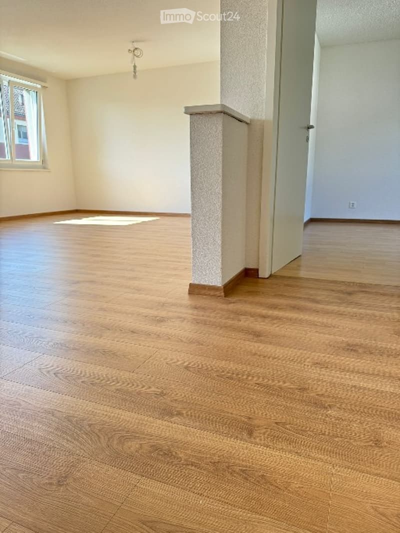 an empty room with wooden flooring, white walls, a window, and an open door