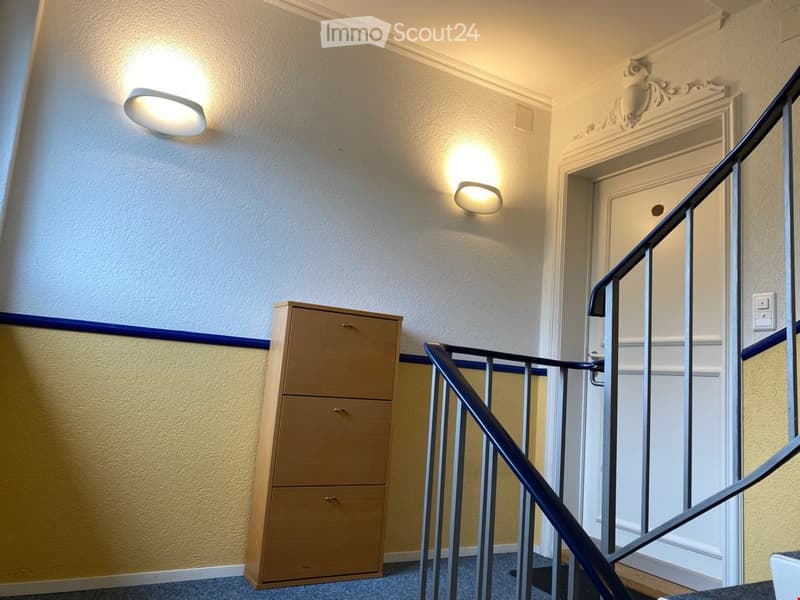 Hallway with a wooden filing cabinet, modern wall-mounted lights, and a staircase with a metal railing.
