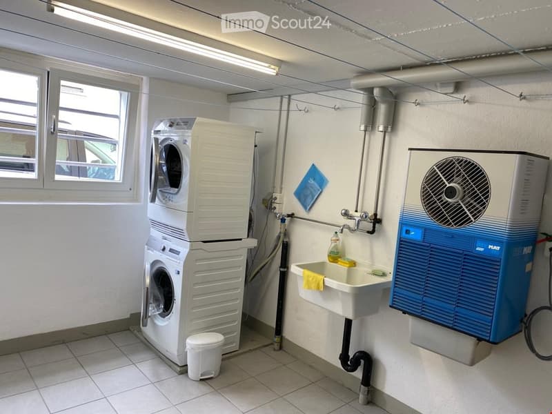 Utility bathroom with a stacked washing machine, sink, and ventilation unit.