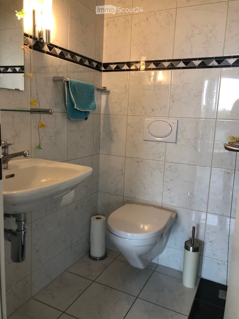 Modern bathroom with marble tiles, a white sink, a toilet, a towel, and a toilet brush holder.