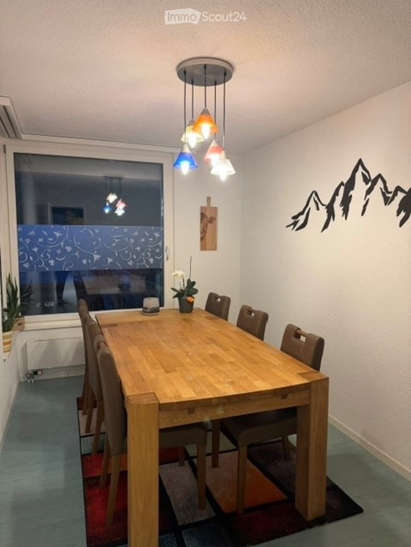 Dining room with a wooden table, six chairs, a flower pot, wall art, and a potted plant near the window.