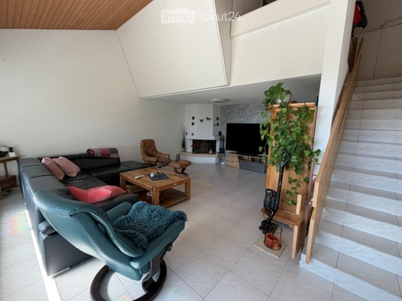 Modern living room with a black sectional sofa, coffee table, armchairs, fireplace, TV, and a plant near the staircase.