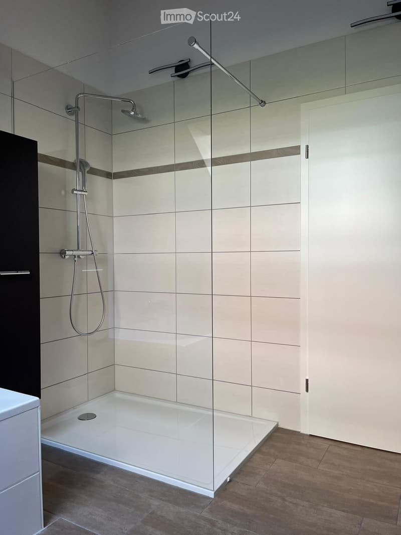 Modern bathroom with a glass-enclosed shower, tiled walls, and a sleek showerhead with multiple spray options.