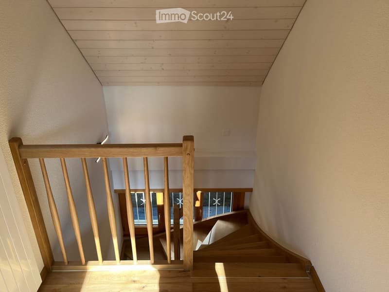Wooden staircase with a wooden railing and light-colored walls, leading to a lower level with a window and door visible at the bottom.