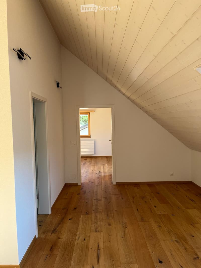 Empty hallway with wooden flooring, white walls, and a slanted wooden ceiling. Two doors lead to adjacent rooms, one with a visible window.