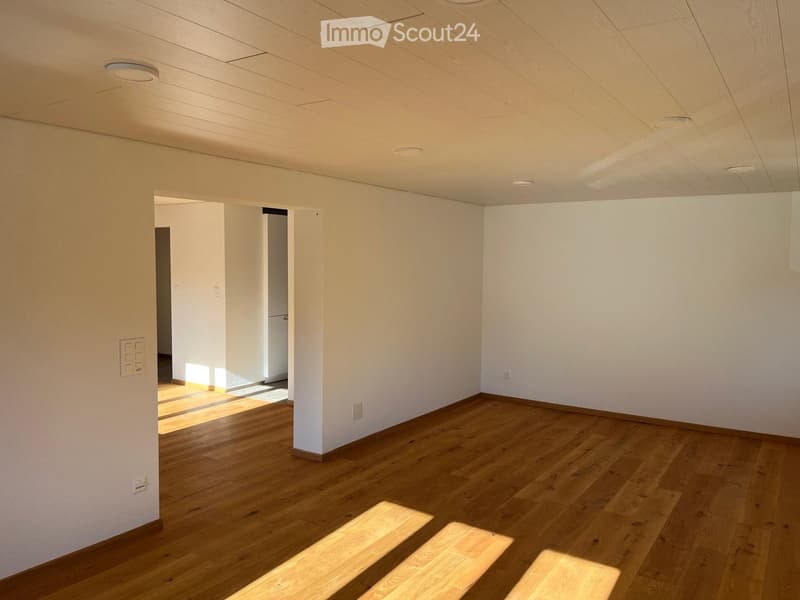 Empty room with light wooden flooring, white walls, and recessed ceiling lighting. The room has an open doorway leading to another space.