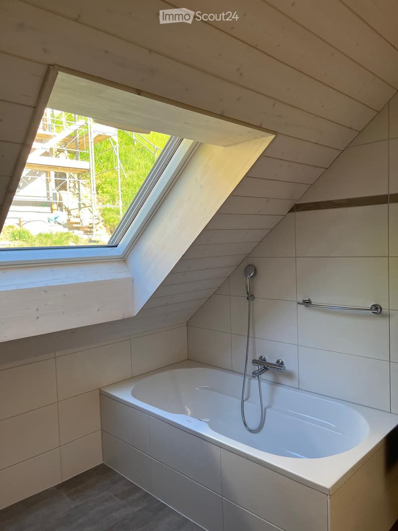 Modern bathroom with a white bathtub, wooden walls, and a skylight window above the tub.