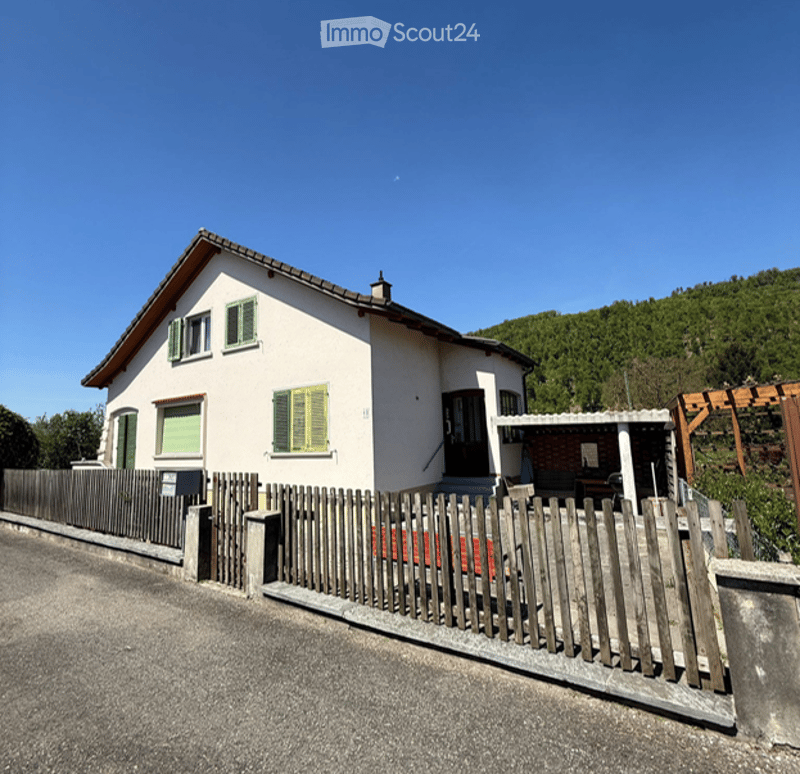 Single-story house with white exterior, green shutters, and a wooden fence surrounding the property.