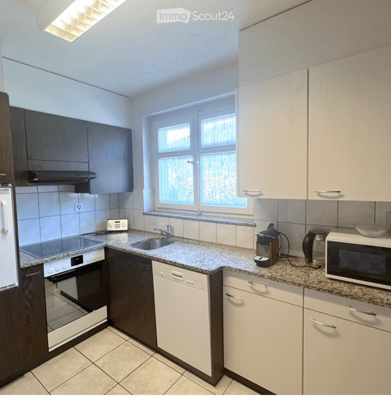 Modern kitchen with white cabinets, granite countertops, stainless steel appliances, and a large window providing natural light.