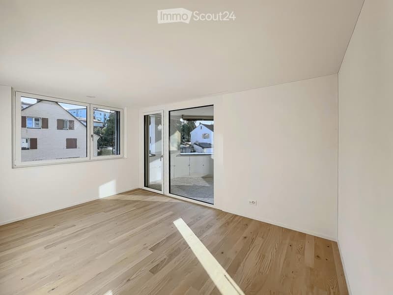 Empty room with light wooden flooring, white walls, large windows, and sliding glass doors leading to an outdoor area.