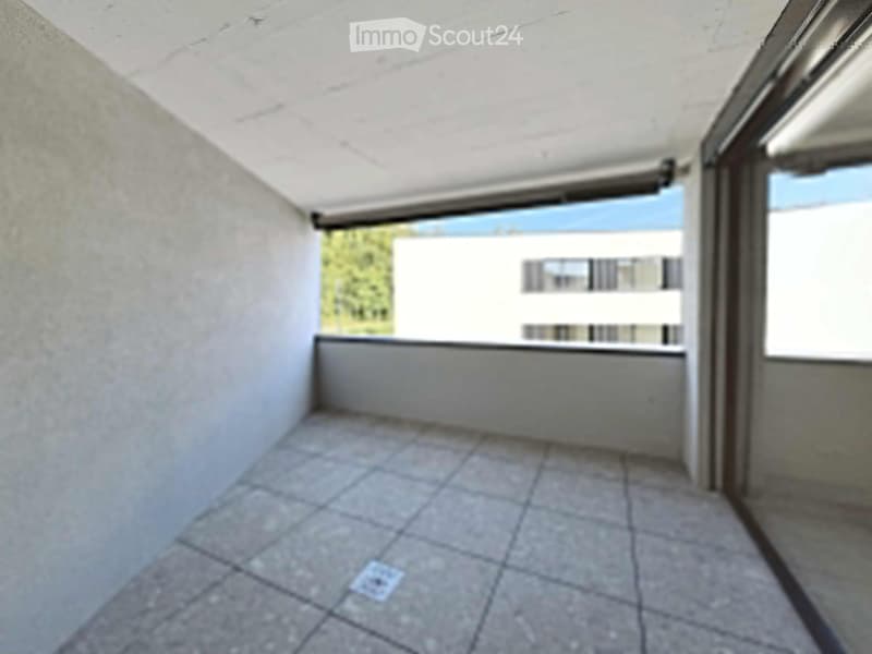 Empty room with tiled floor, white walls, and large windows offering a view of the outside area.