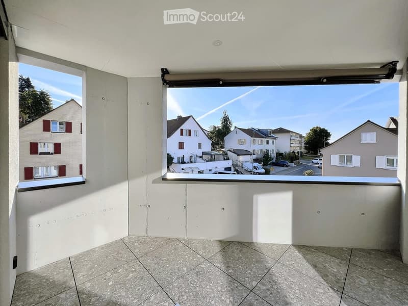 Empty balcony with tiled floor, white walls, and large windows offering a view of the neighborhood.