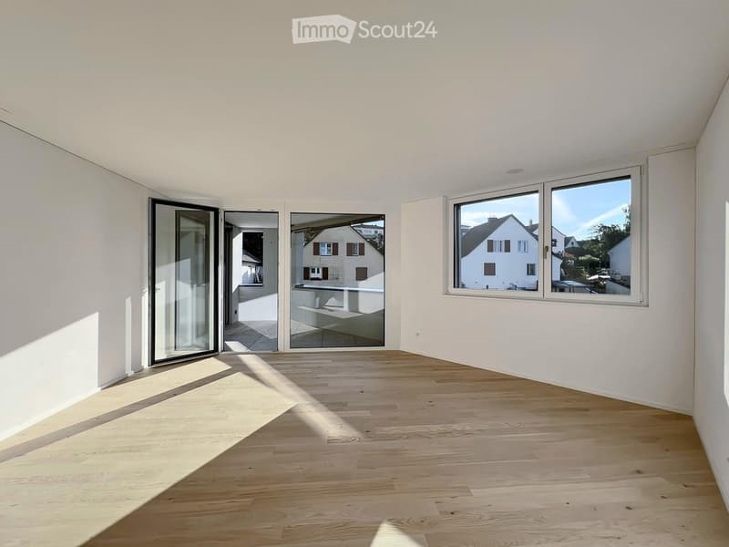 Empty room with light wooden flooring, white walls, large windows, and sliding glass doors leading to a balcony.