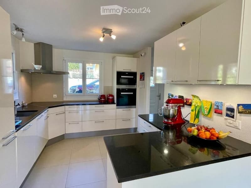 Modern kitchen with white cabinets, black countertops, stainless steel appliances, and a red stand mixer on the counter.