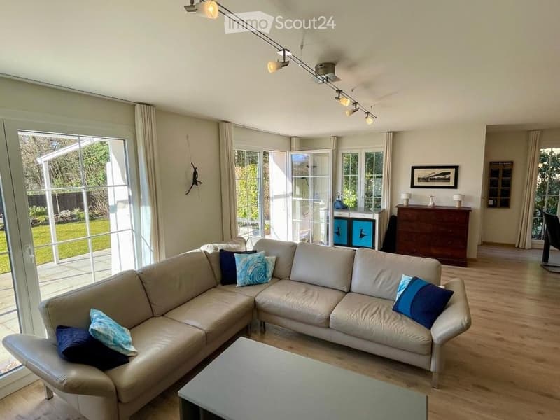 Modern living room with large windows, light-colored leather sofa, coffee table, side table, and decorative pillows.