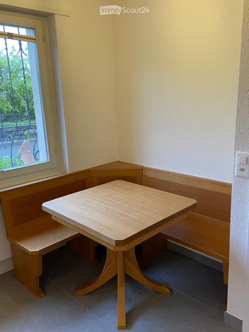 Corner seating area with a built-in bench and a small wooden table, near a window with a view of greenery.