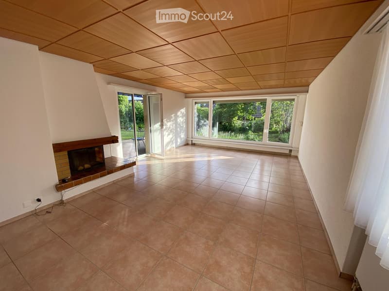 Empty room with tiled floor, fireplace, large windows, and sliding glass doors leading to a garden.