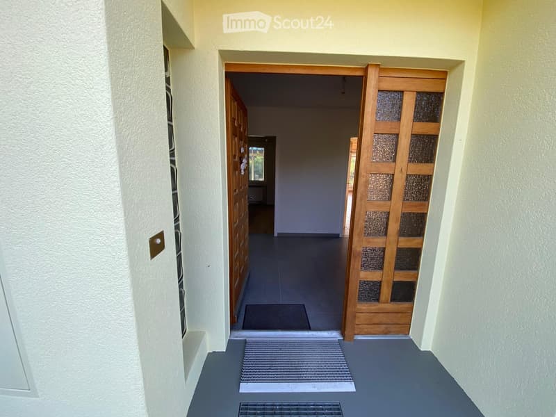A clean, well-lit hallway with a tiled floor, white walls, and wooden doors leading to other rooms.