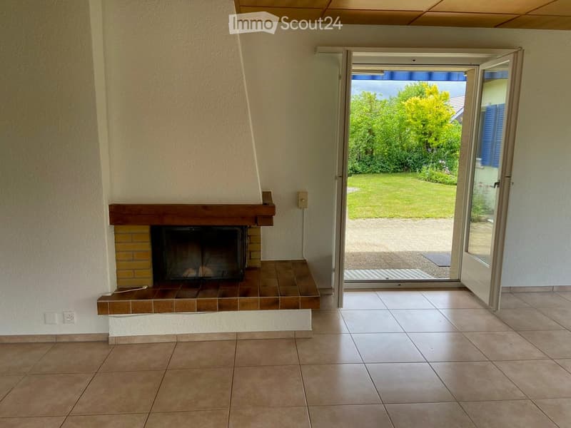 Living room with tiled floor, fireplace, and sliding glass door leading to a garden.