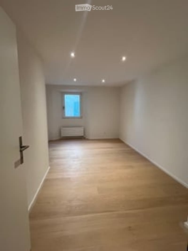 Completely empty room with wooden flooring, white walls, and a single window with a radiator beneath it. No furniture or equipment is present.