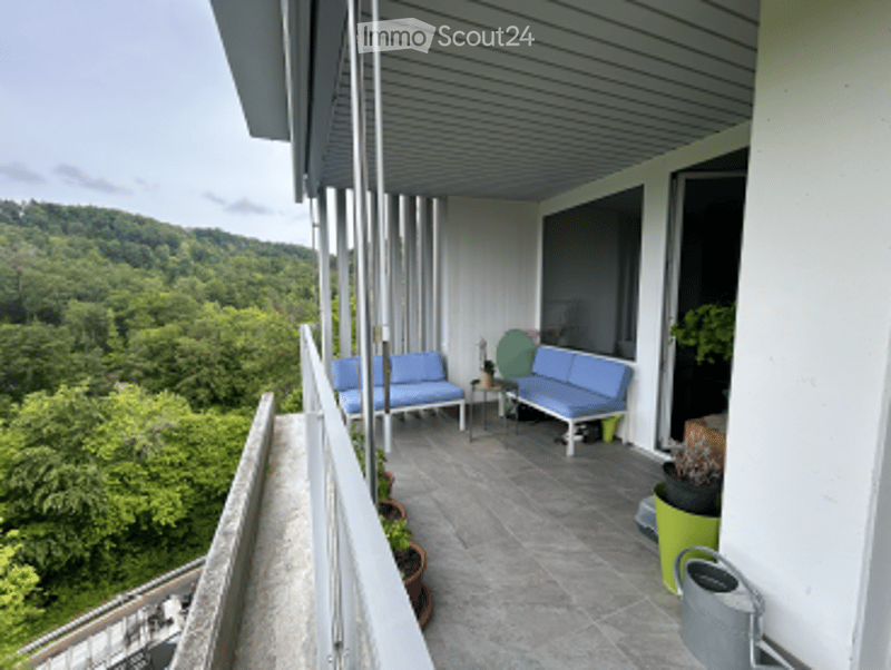 Balcony with a view of a green, hilly landscape, featuring a blue sofa, small table, and potted plants.
