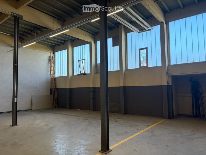 Empty industrial-style room with concrete floor, exposed metal beams, large windows, and a ladder leaning against the wall.