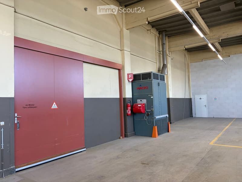 Industrial space with a large red garage door, electrical equipment, and a fire extinguisher.