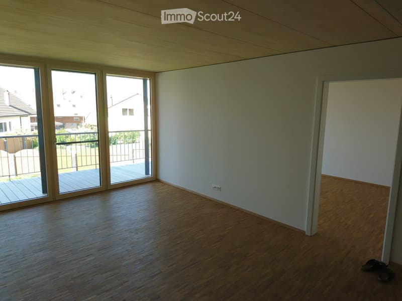 Empty room with wooden flooring, white walls, large sliding glass doors leading to a balcony, and a visible electrical outlet on the wall.