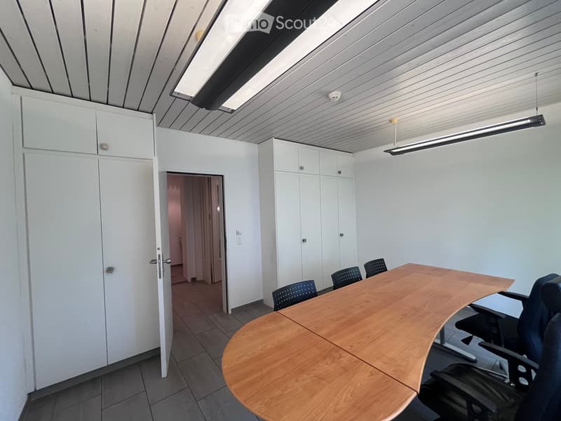 An empty room with a large desk, chairs, and cabinets. The room has white walls and a ceiling with lights.