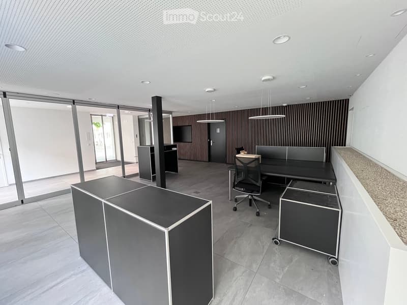 Modern office space with a large desk, a chair, a monitor, and storage units. The room has a sleek design with gray and white elements.