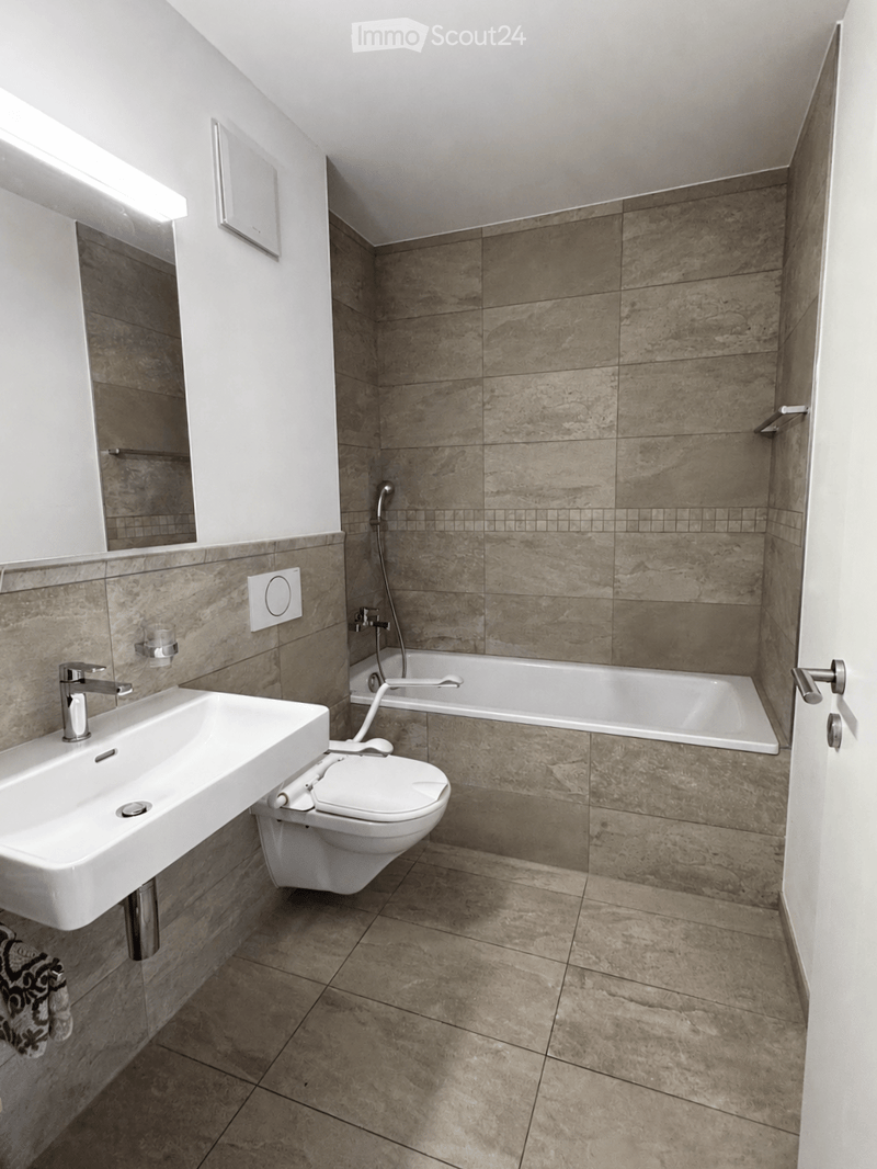 Modern bathroom with beige marble tiles, a white sink, toilet, bathtub, and a large mirror with built-in lighting.